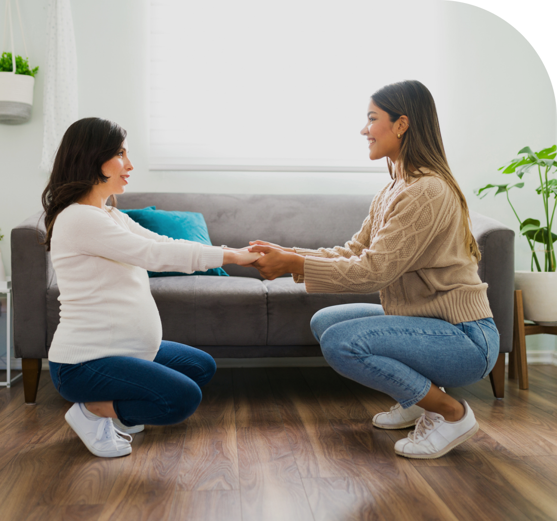Pregnant woman and friend holding hands, smiling.